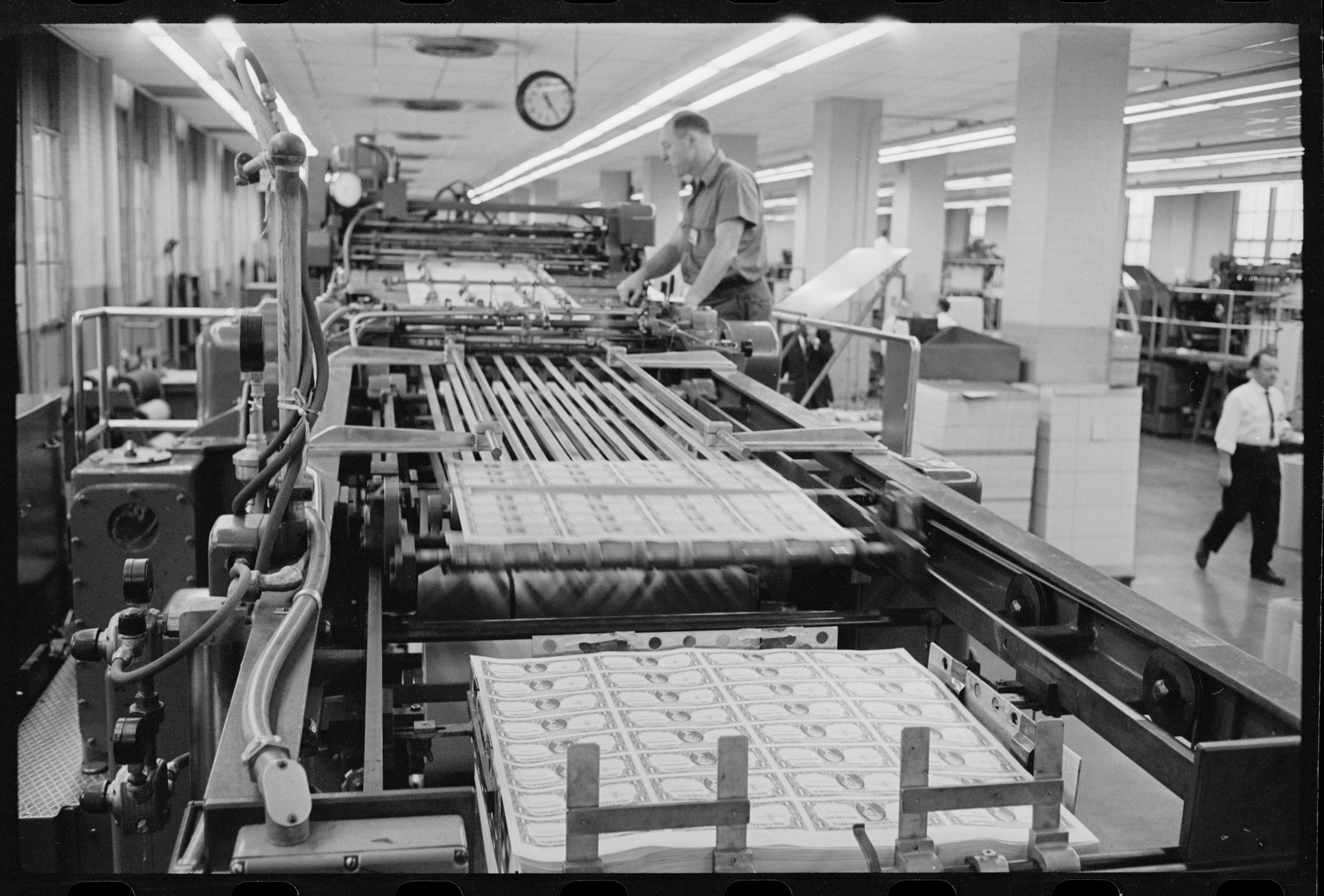 A press operator at the U.S. Bureau of Engraving and Printing, with sheets of currency moving through the machinery.