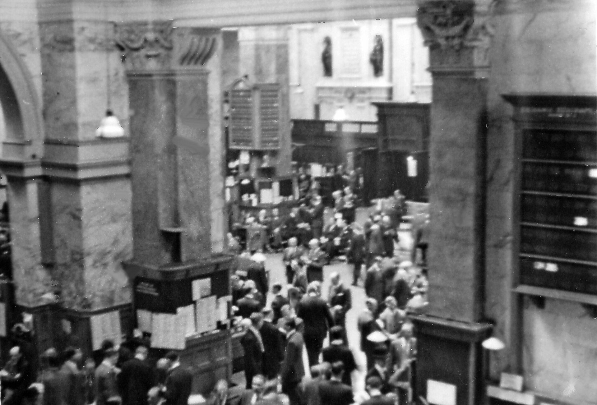 The London Stock Exchange trading floor in 1955 with brokers gathered under tall windows.