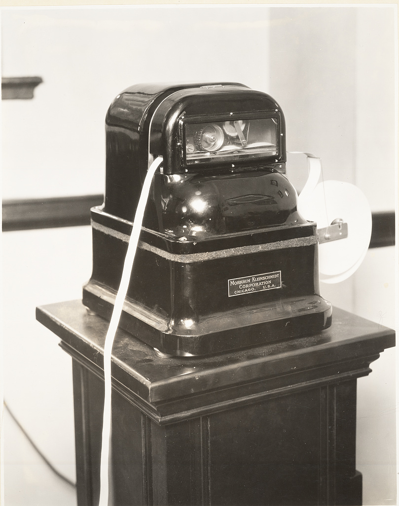 A 1926 Morkrum-Kleinschmidt ticker instrument with a strip of market tape emerging from it.